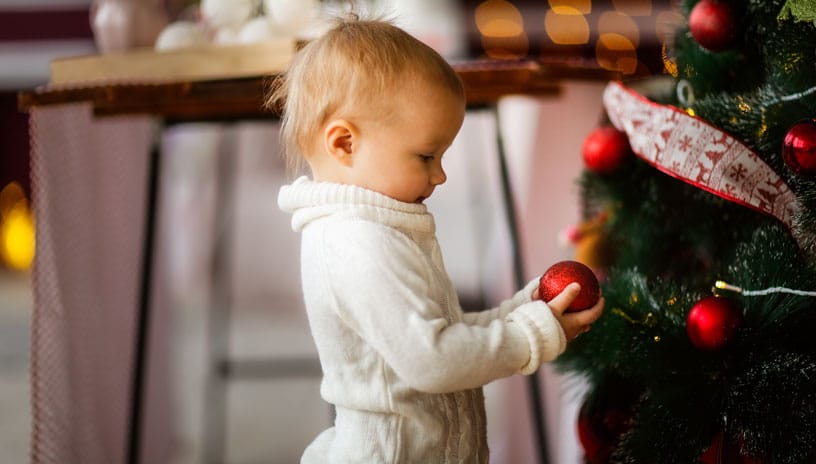 Child admiring Christmas ornament on tree