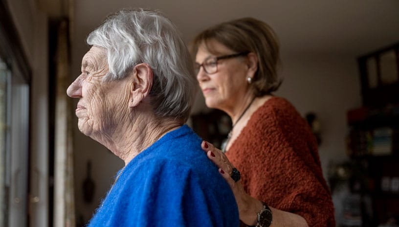 two elderly friends standing looking out of the window